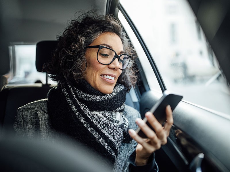 Woman sitting in back seat of a car on her phone.