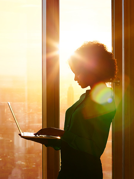 Black professional woman standing at window with laptop