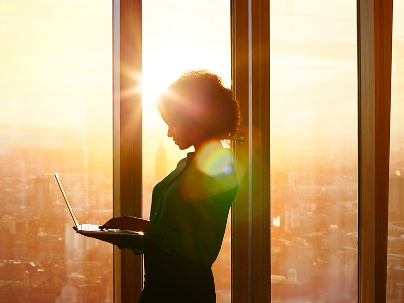 Black professional woman standing at window with laptop