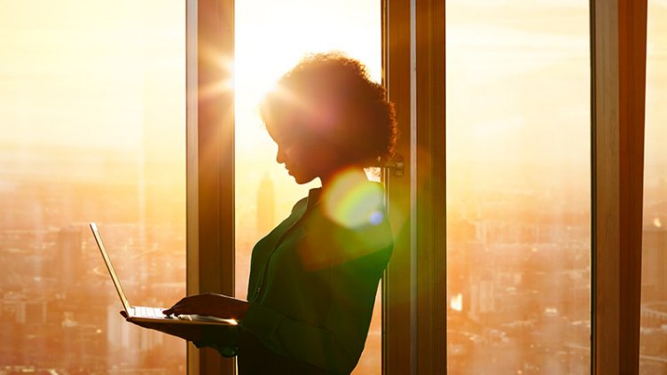Black professional woman standing at window with laptop