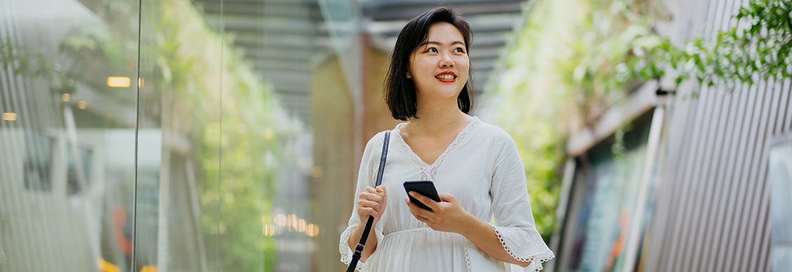 a smiling woman holding smartphone and looking away in a green building