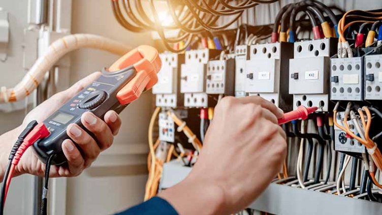 Electrician engineer uses a multimeter to test the electrical installation and power line current in an electrical system control cabinet
