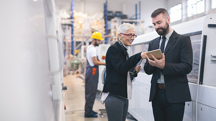 Diverse professionals review information on a tablet while facility professional in a hard hat works on machinery