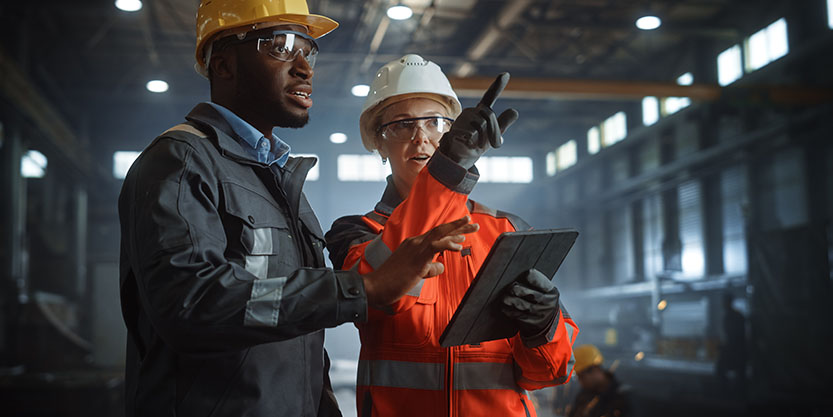 African-American worker talking with Caucasian businesswoman and looking at a tablet in a factory