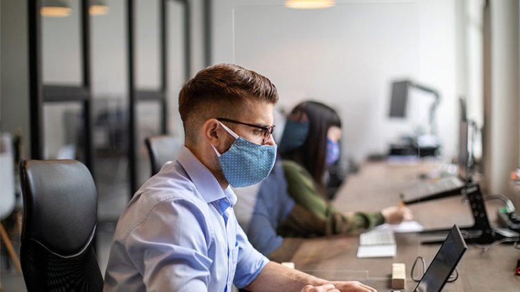 Employees working having face mask on in office workspace during COVID-19