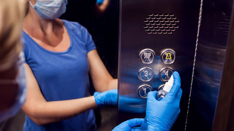 Woman sanitizing the buttons inside the elevator