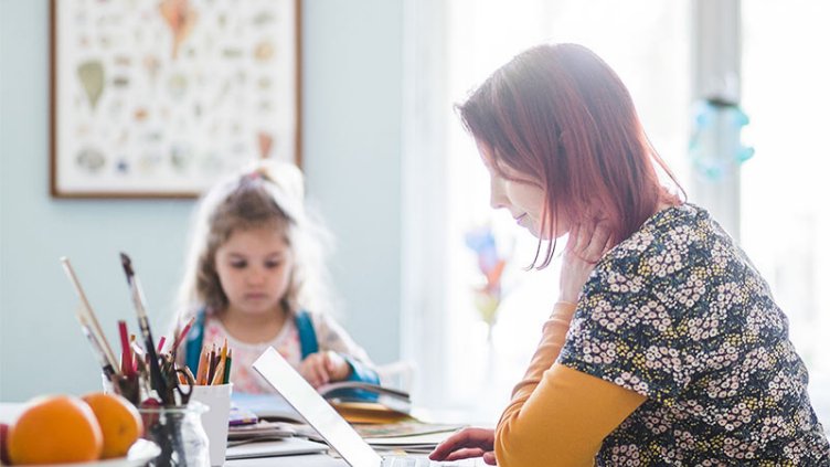 A women working from home on laptop and her daughter sitting nearby and studying