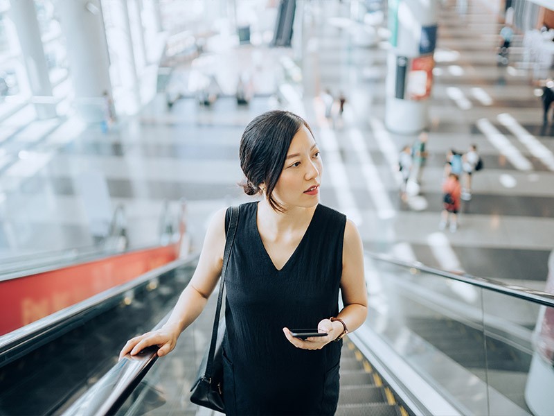 A girl holding mobile and going on escalator