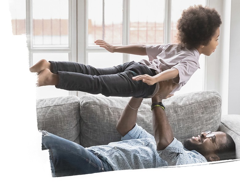 father laying on sofa at home playing with child​