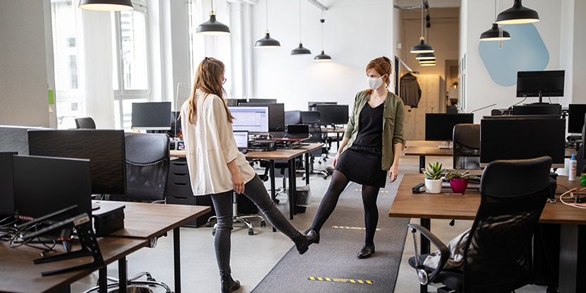 Two women in the office greeting each other with a foot bump