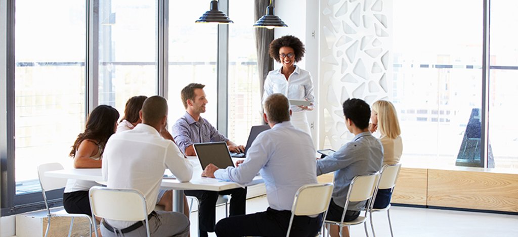 team members listen to businesswoman giving meeting