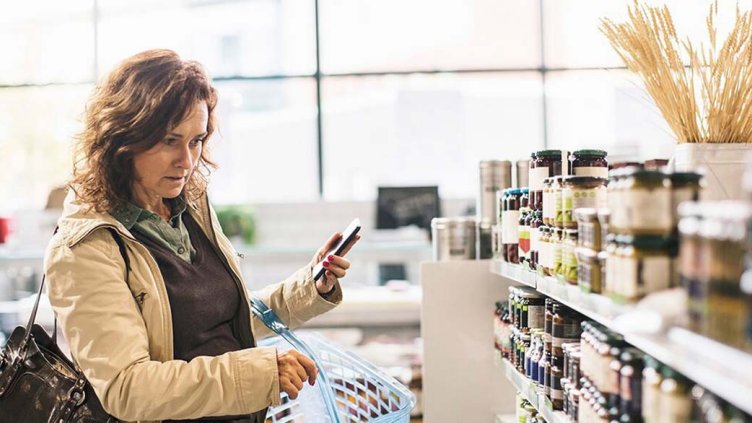 Woman holding smartphone while shopping in the supermarket