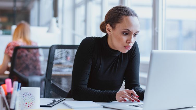 Picture of a professional lady working on her laptop sitting at the workspace inside the office