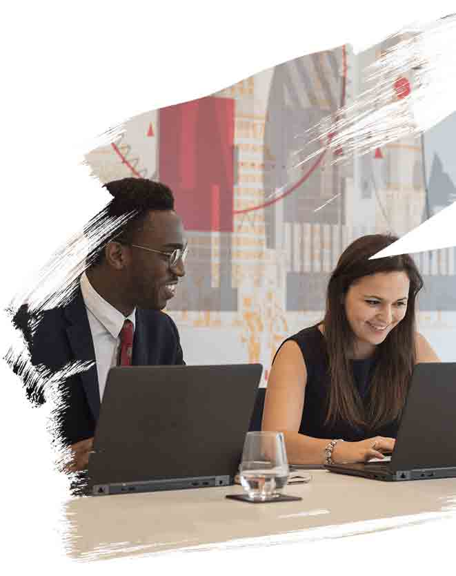 Picture of two employees smiling while working together on there laptops