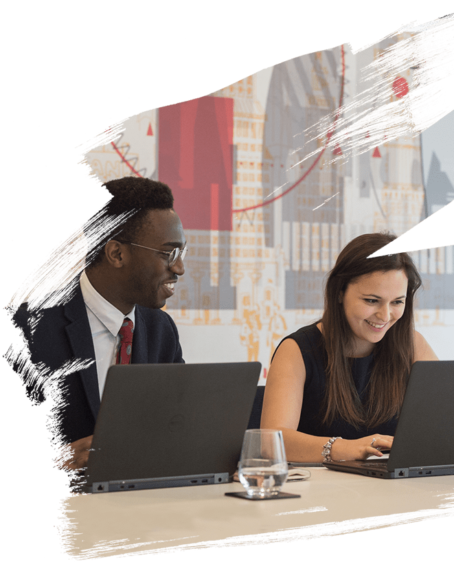 Picture of two employees smiling while working together on there laptops