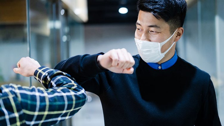 Two colleagues in face masks avoid handshake and greeting with bumping elbows at office workplace