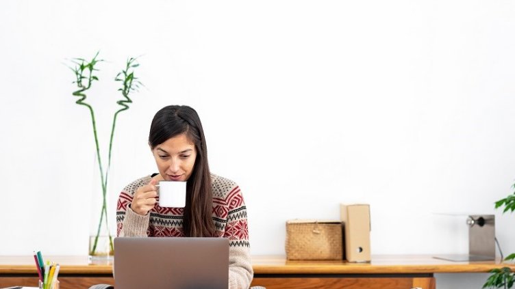Woman drinking coffee and working on laptop at home