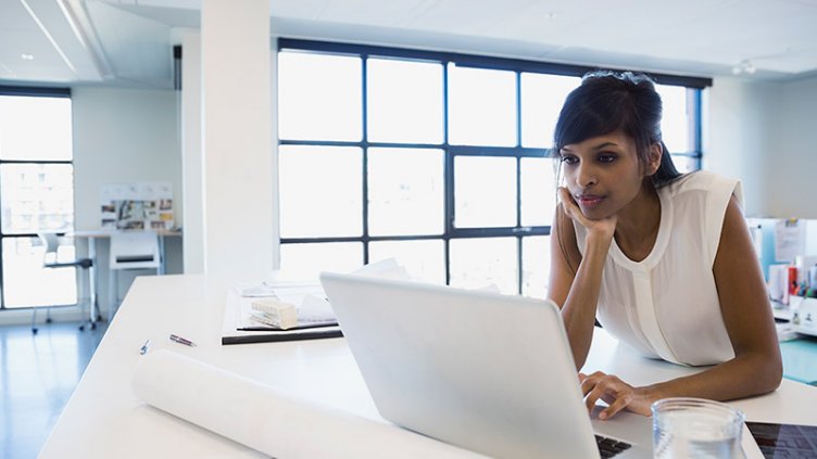 Woman working at desk in office with her laptop and papers in front of her